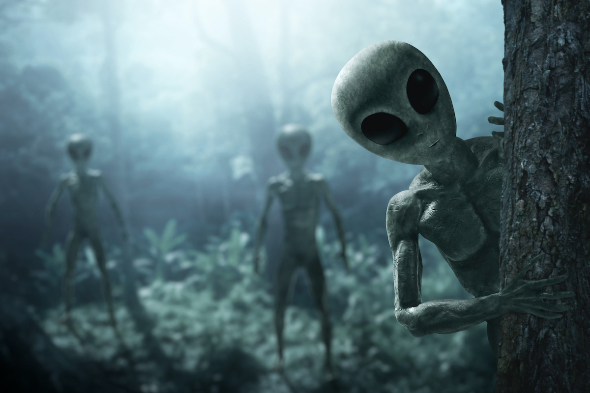 Alien creatures peek out from behind trees in the forest
